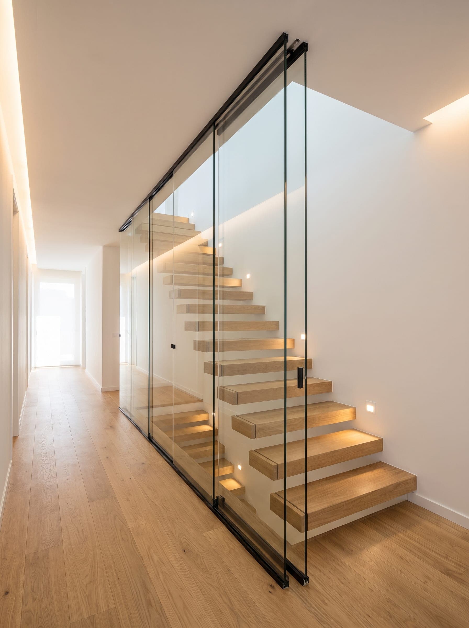 A frameless glass partition enclosing a stairwell in a hallway