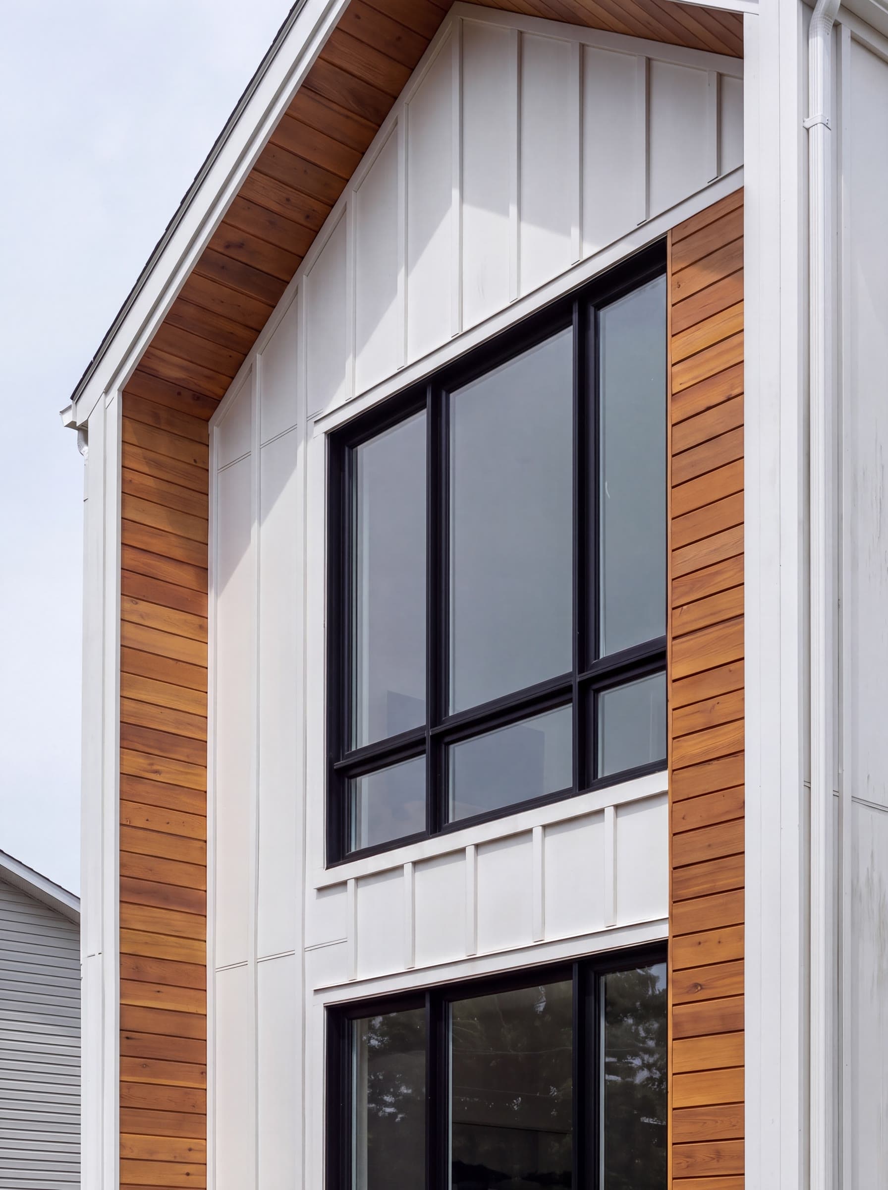 Fenêtres hybrides noires sur une façade moderne à planches blanches et accents de cèdre