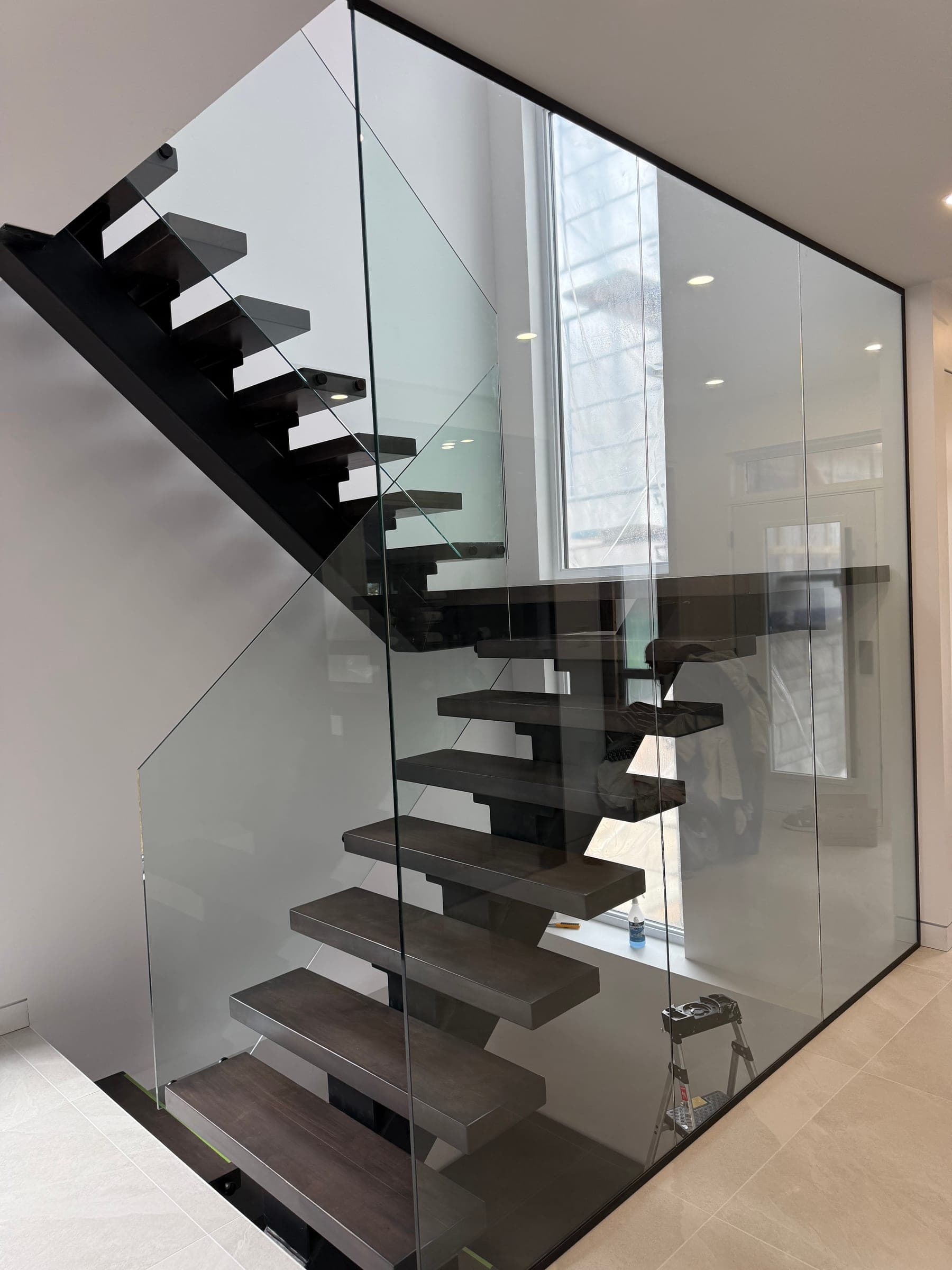 A suspended dark-wood staircase enclosed in frameless glass across two storeys