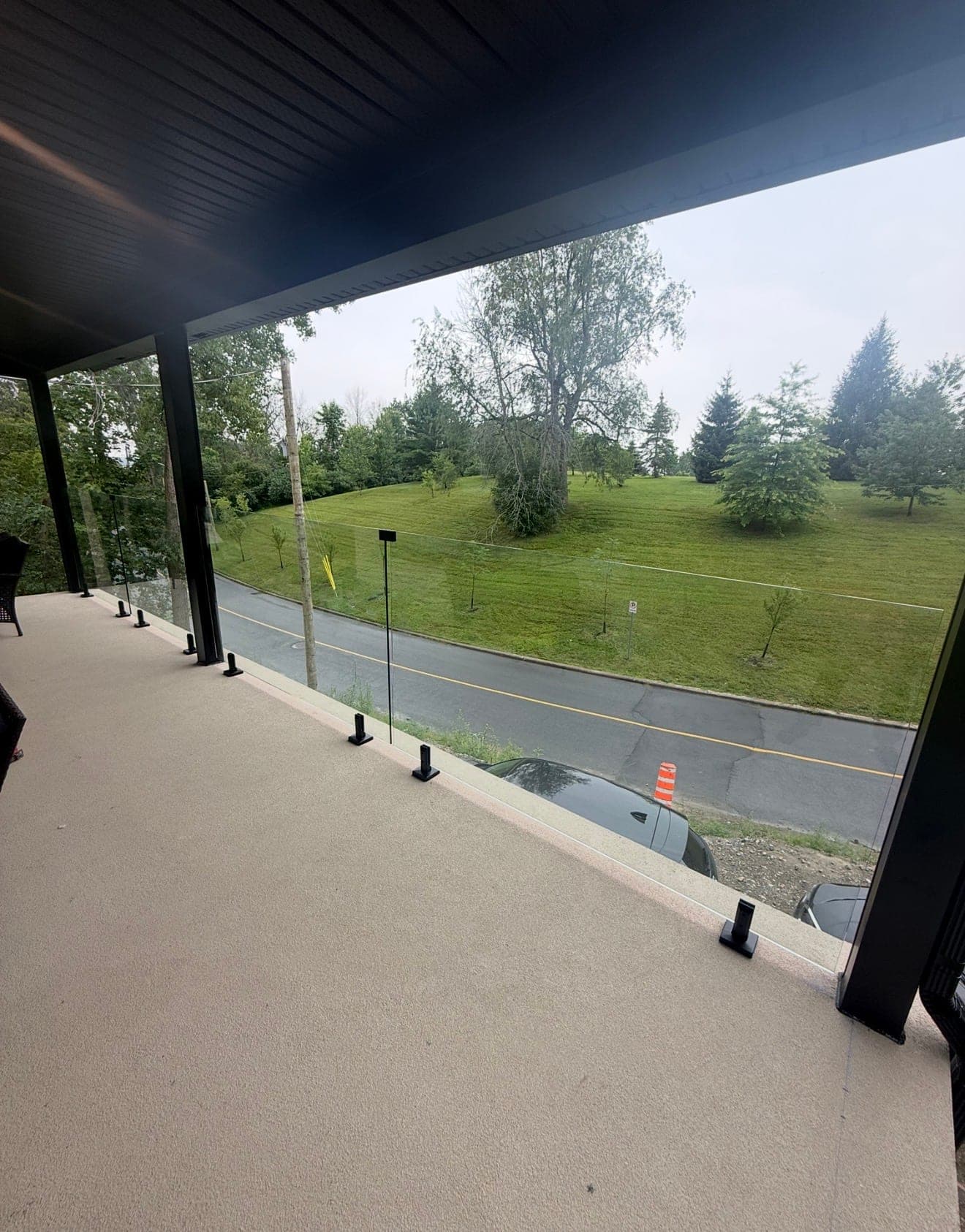 Garde-corps de balcon en verre sur poteaux, donnant sur un grand terrain vert